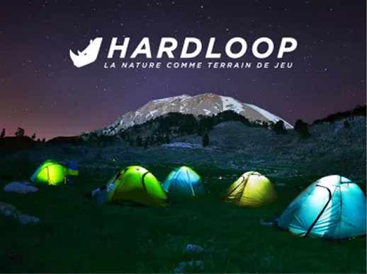 Tents lit up at a bivouac in front of a snowy summit at night, with the Hardloop logo