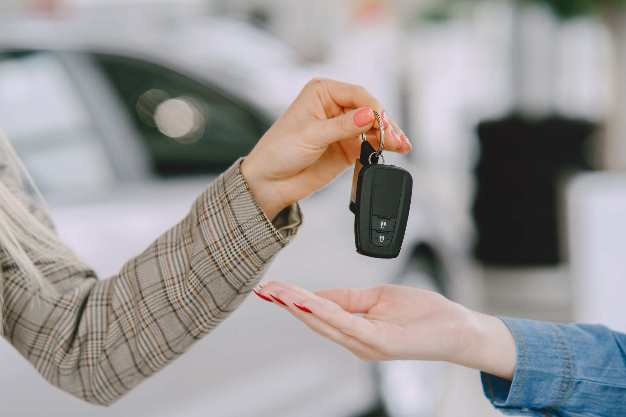 One hand passing car keys to another, in front of a vehicle at a dealership