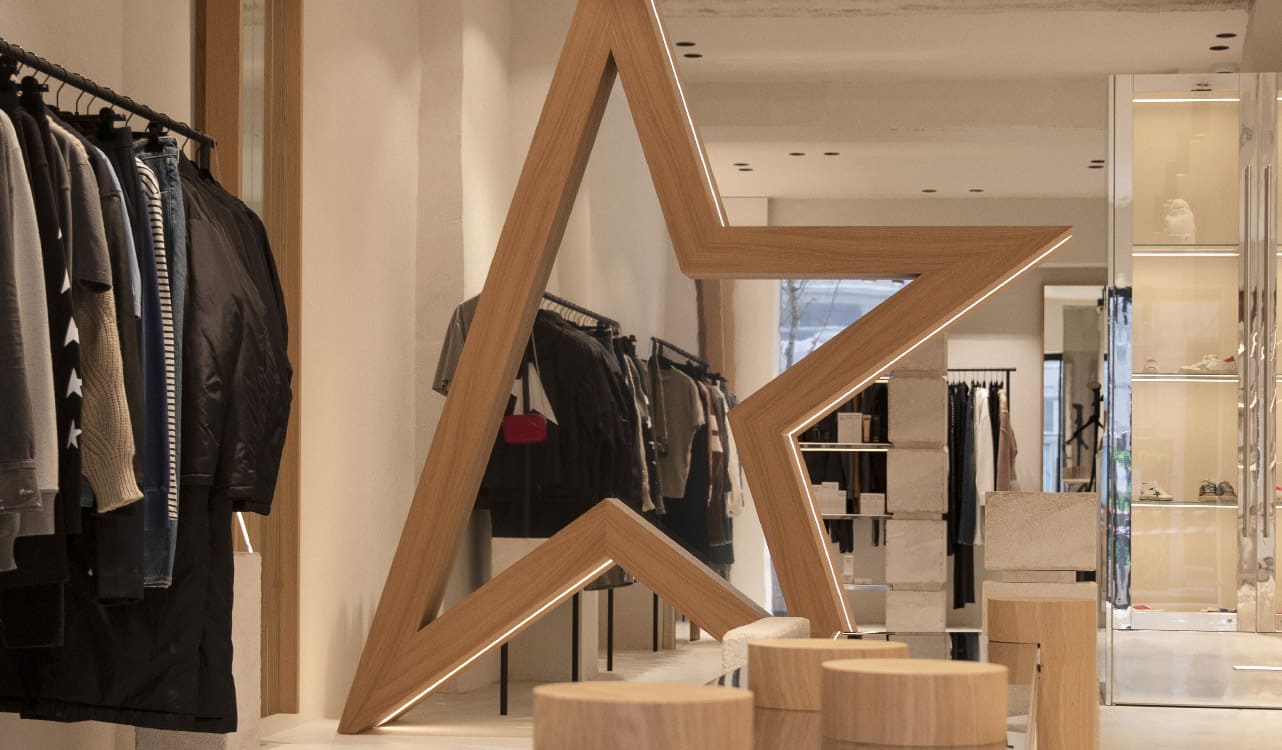 Inside a Lulli sur la Toile shop: a central display case of leather goods and accessories, under patinated metal pendant lights