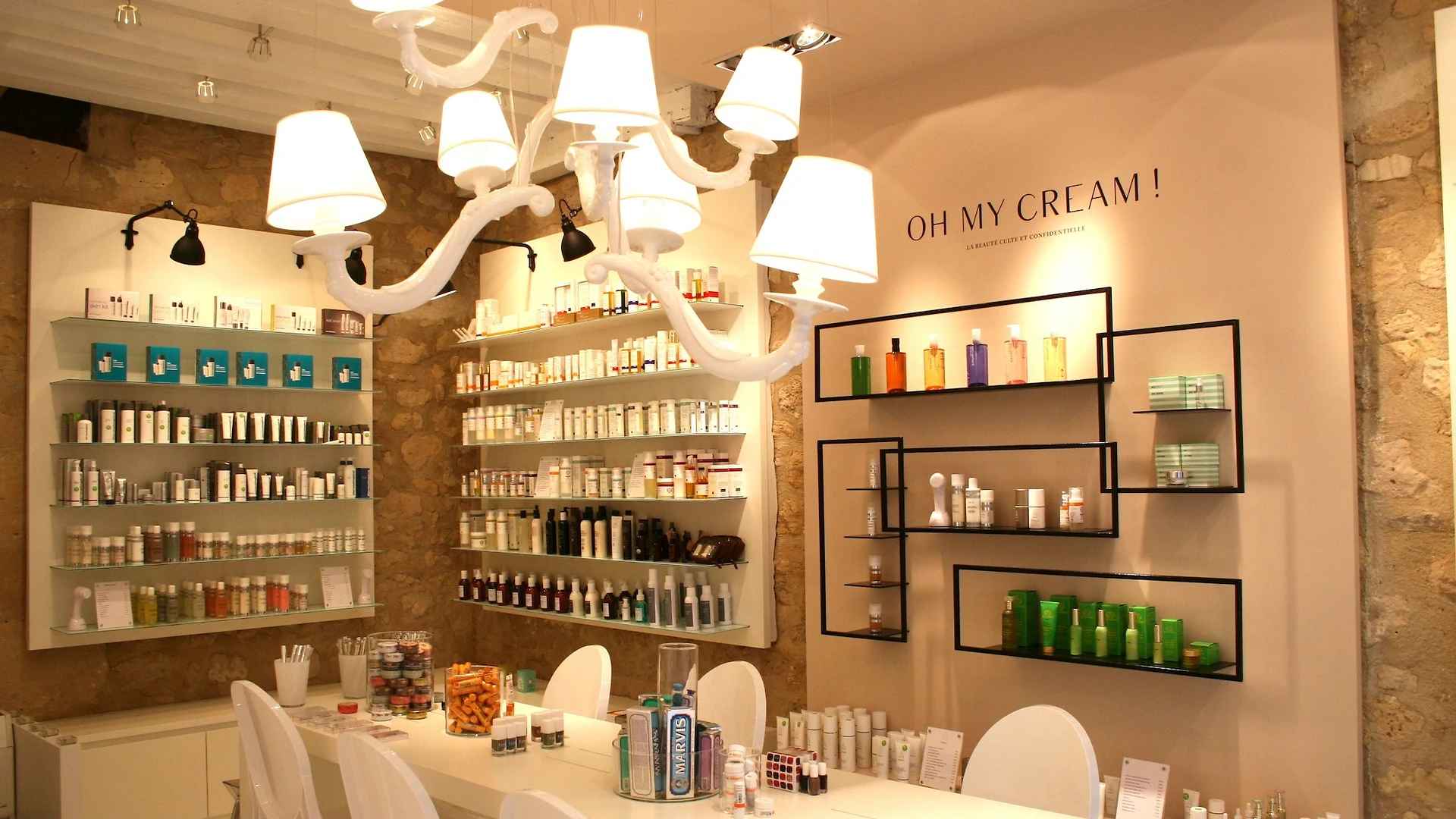 Inside an Oh My Cream shop: shelves of skincare on a stone wall, under a white chandelier, with the brand name painted on the wall